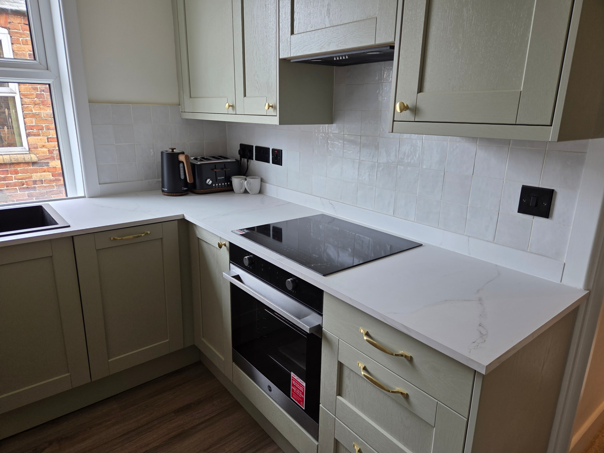 Kitchen with sage-green shaker units, marble-effect worktops, induction hob and brass handles