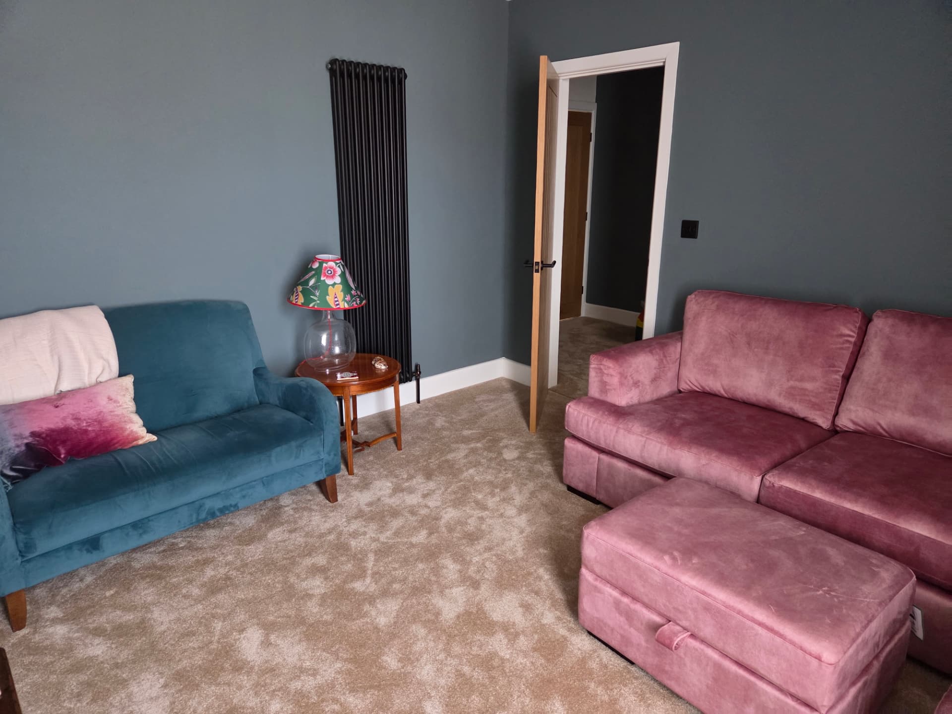 Sitting room with a blue velvet sofa, pink sofa, floral lamp and modern radiator